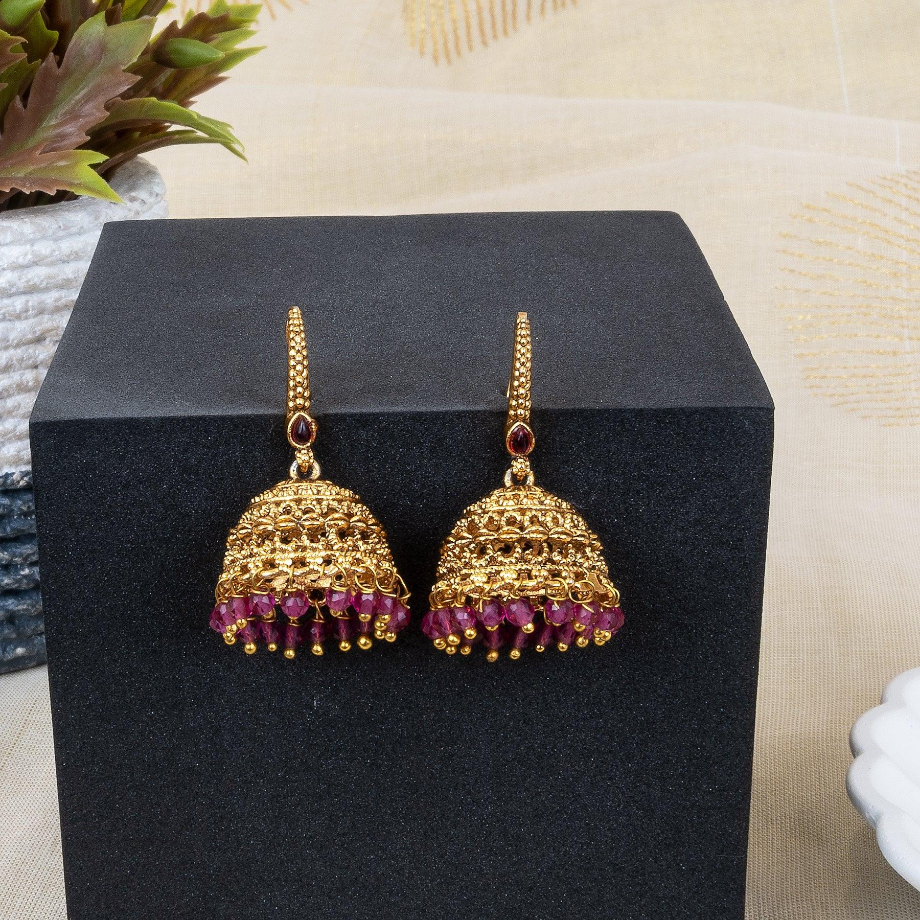 Gold earrings with red gemstones on a black stand