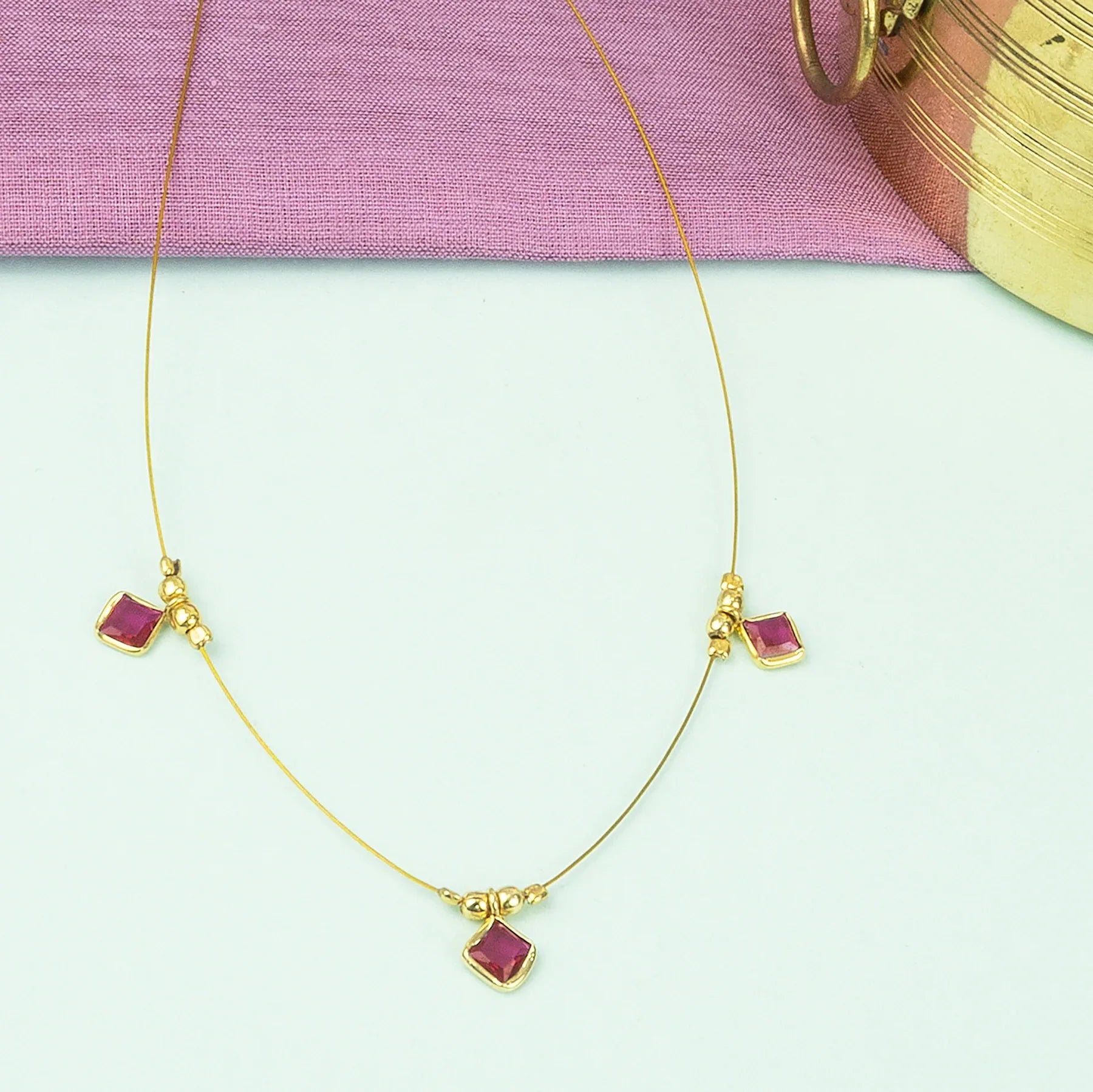 Gold necklace with red gemstones on a light pink fabric background