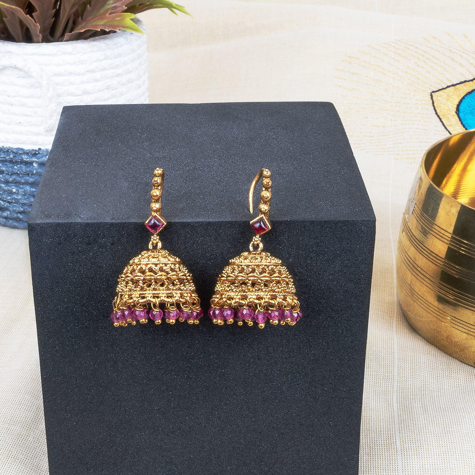 Gold earrings with purple stones on a black stand, with a blurred background