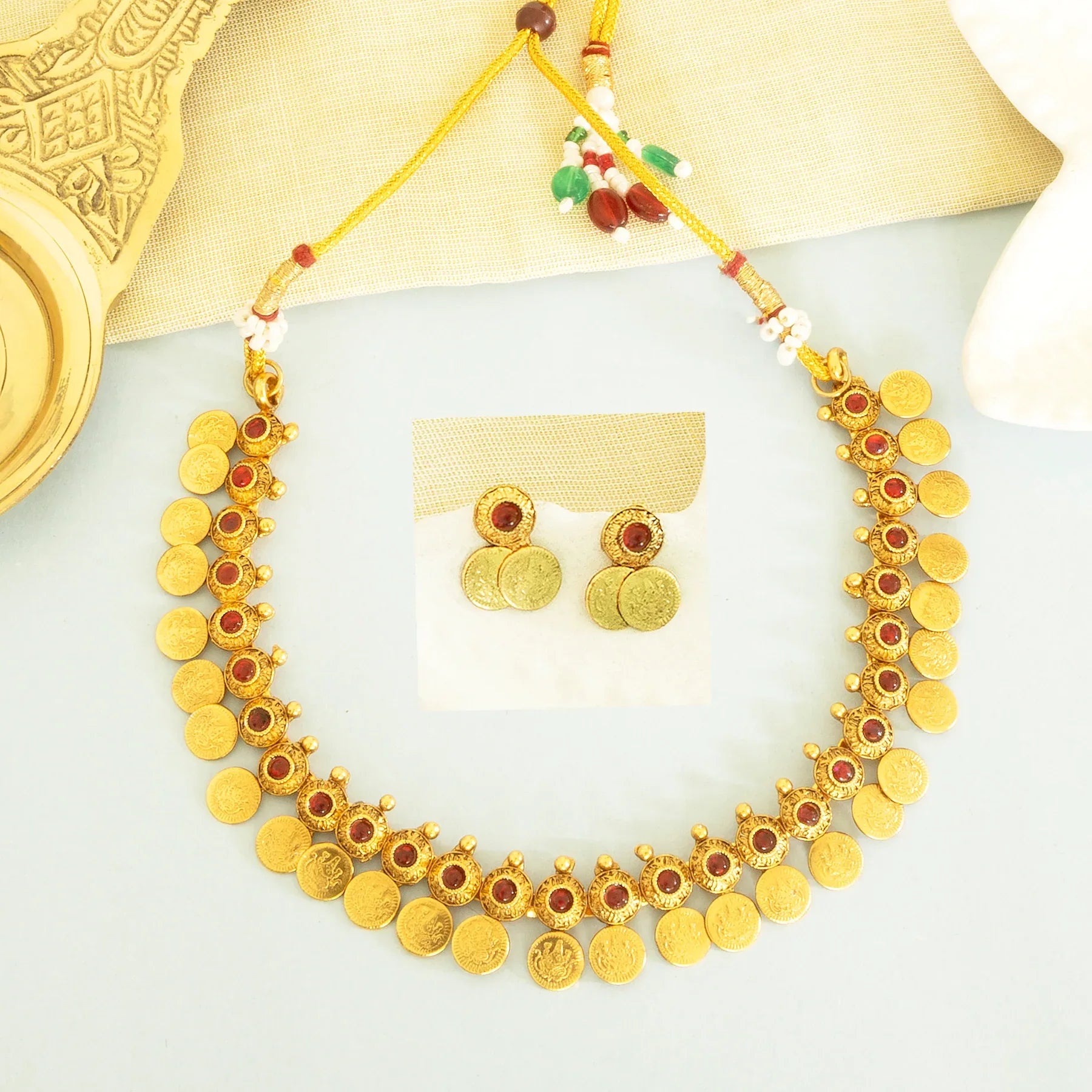 Gold necklace with red stones and matching earrings on a white background