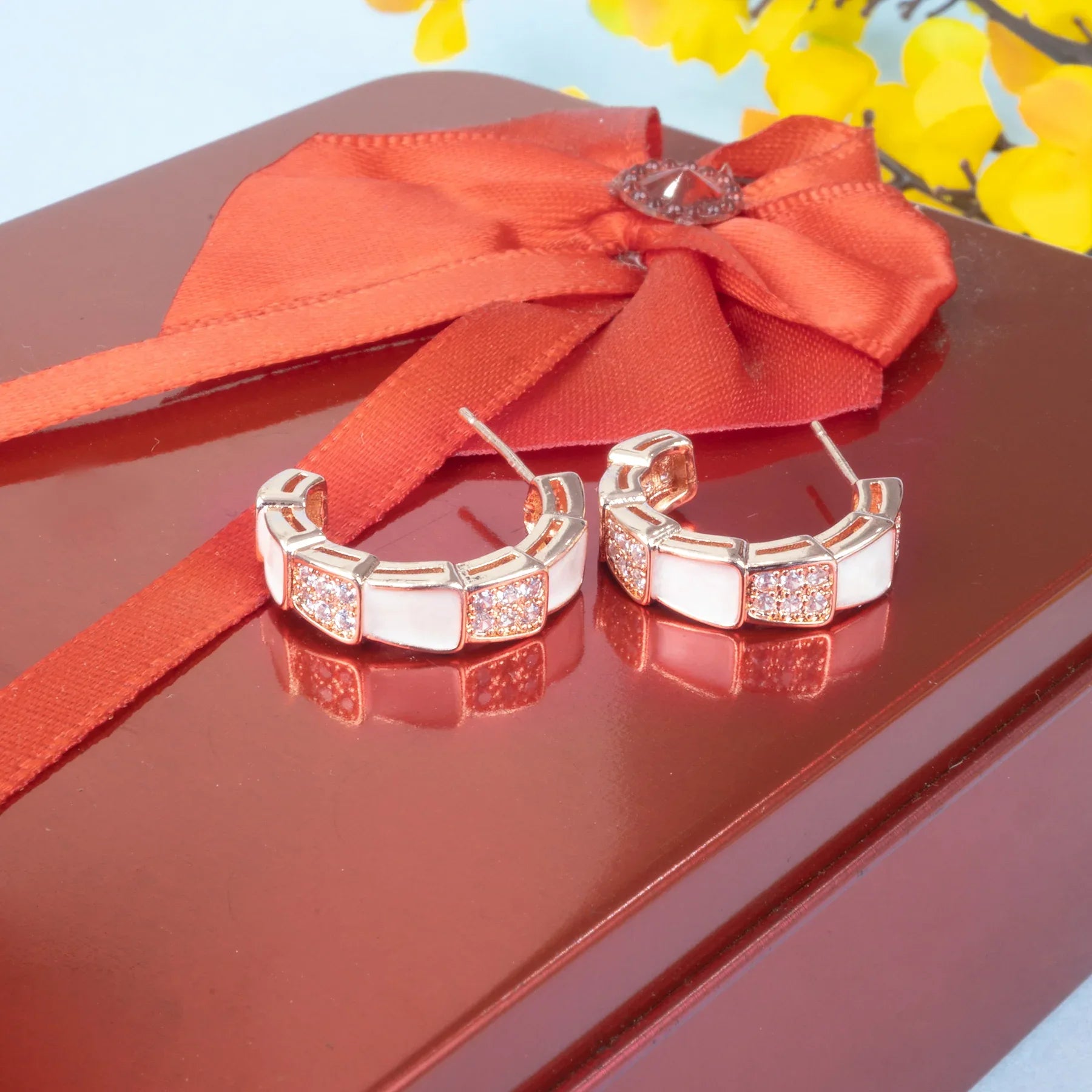 Silver hoop earrings on a red surface with a red ribbon and yellow flowers in the background