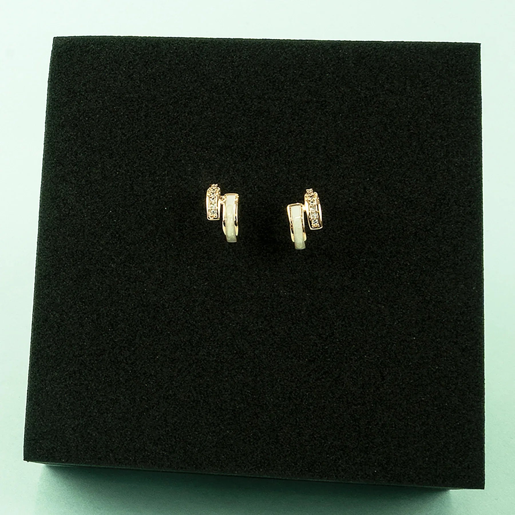 Gold earrings on a black cushion against a light blue background