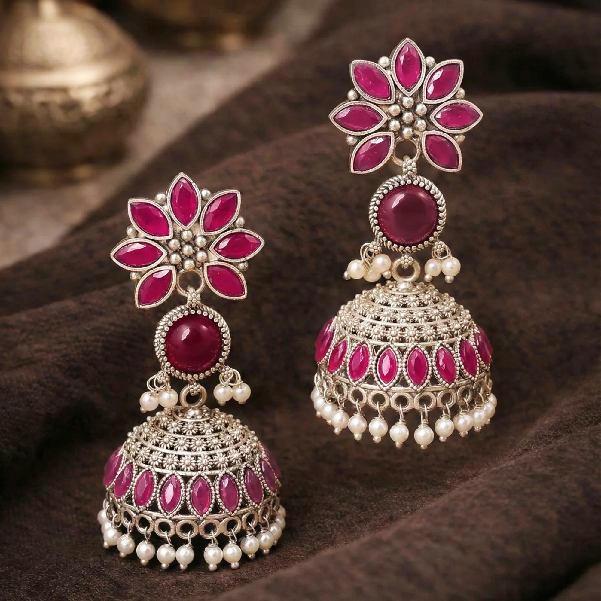 Ornate earrings with pink gemstones and pearl accents on a brown fabric background