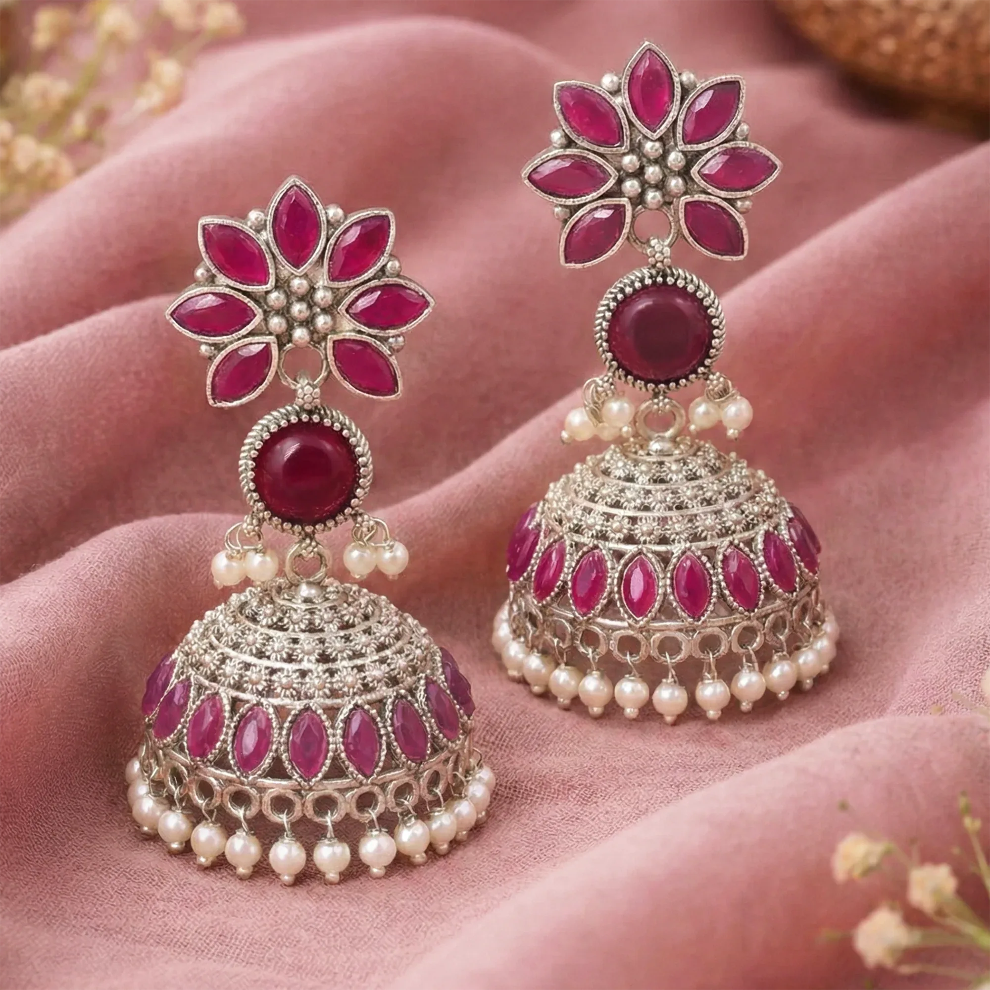 Ornate earrings with pink gemstones and pearl accents on a soft pink fabric background