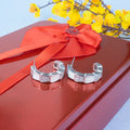 Silver hoop earrings on a red surface with a red ribbon and yellow flowers in the background