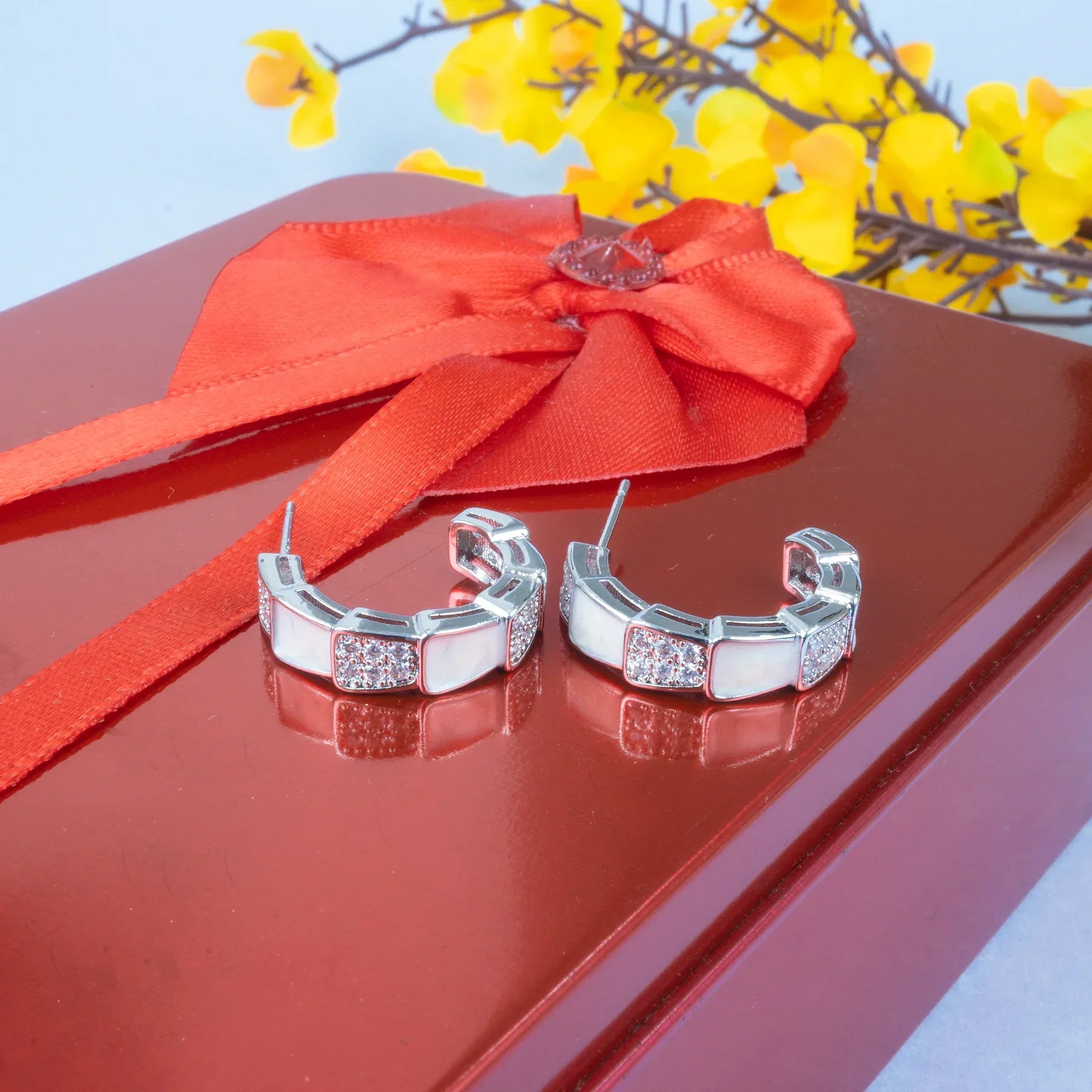 Silver hoop earrings on a red surface with a red ribbon and yellow flowers in the background