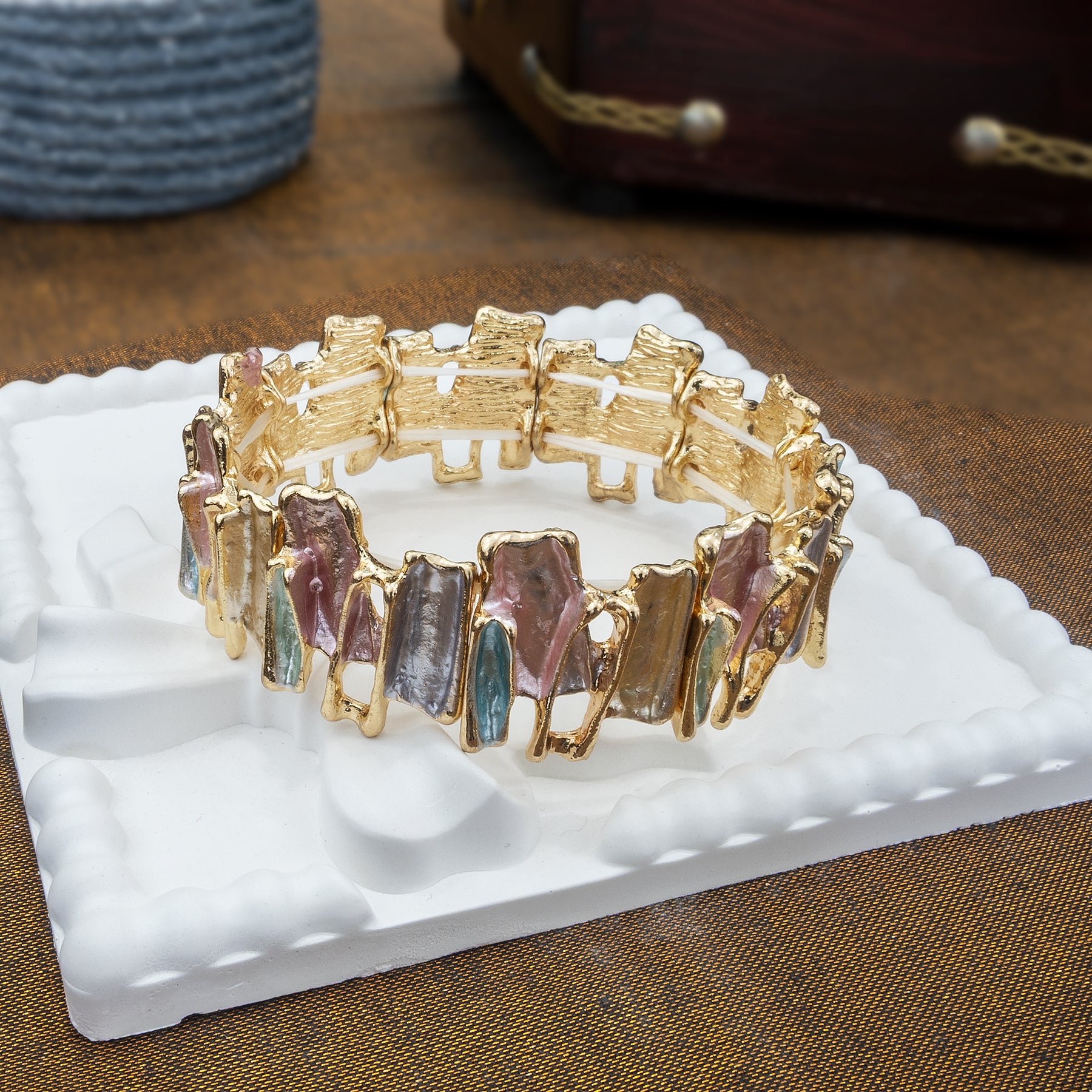 Gold bracelet with multicolored stones on a white stand