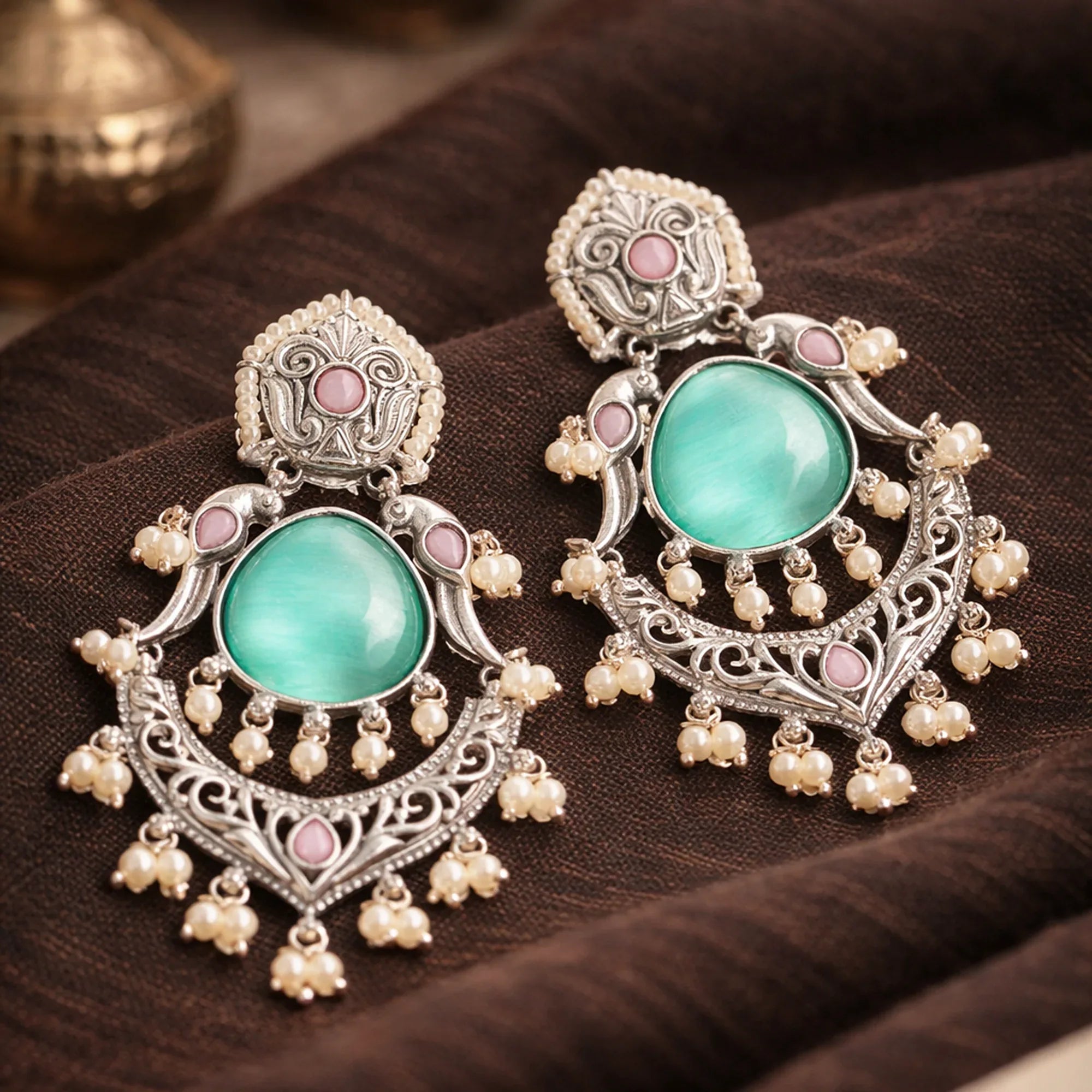 Ornate earrings with turquoise stones and pearl-like elements on a brown fabric background