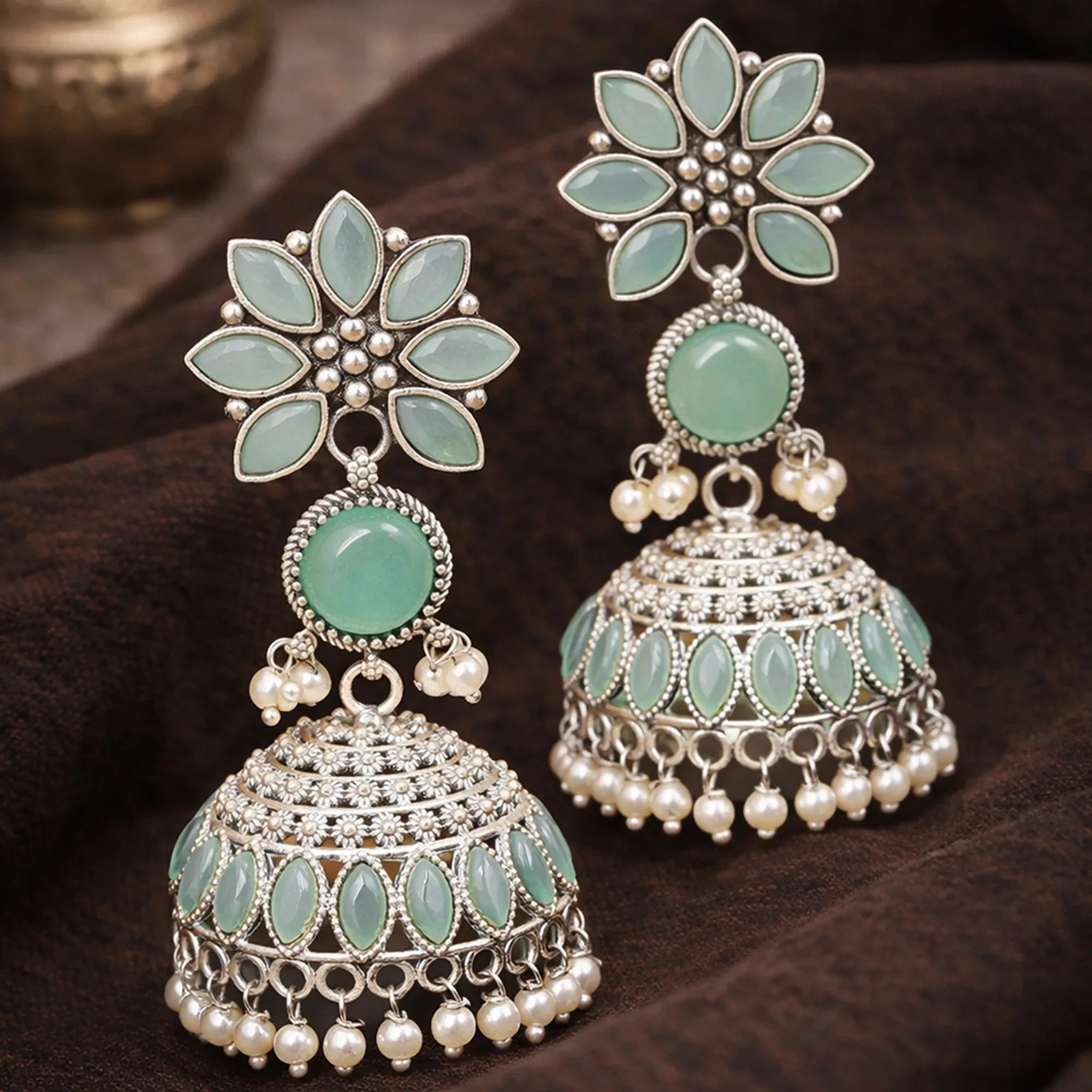 Pair of decorative earrings with green stones and pearl-like beads on a dark fabric background