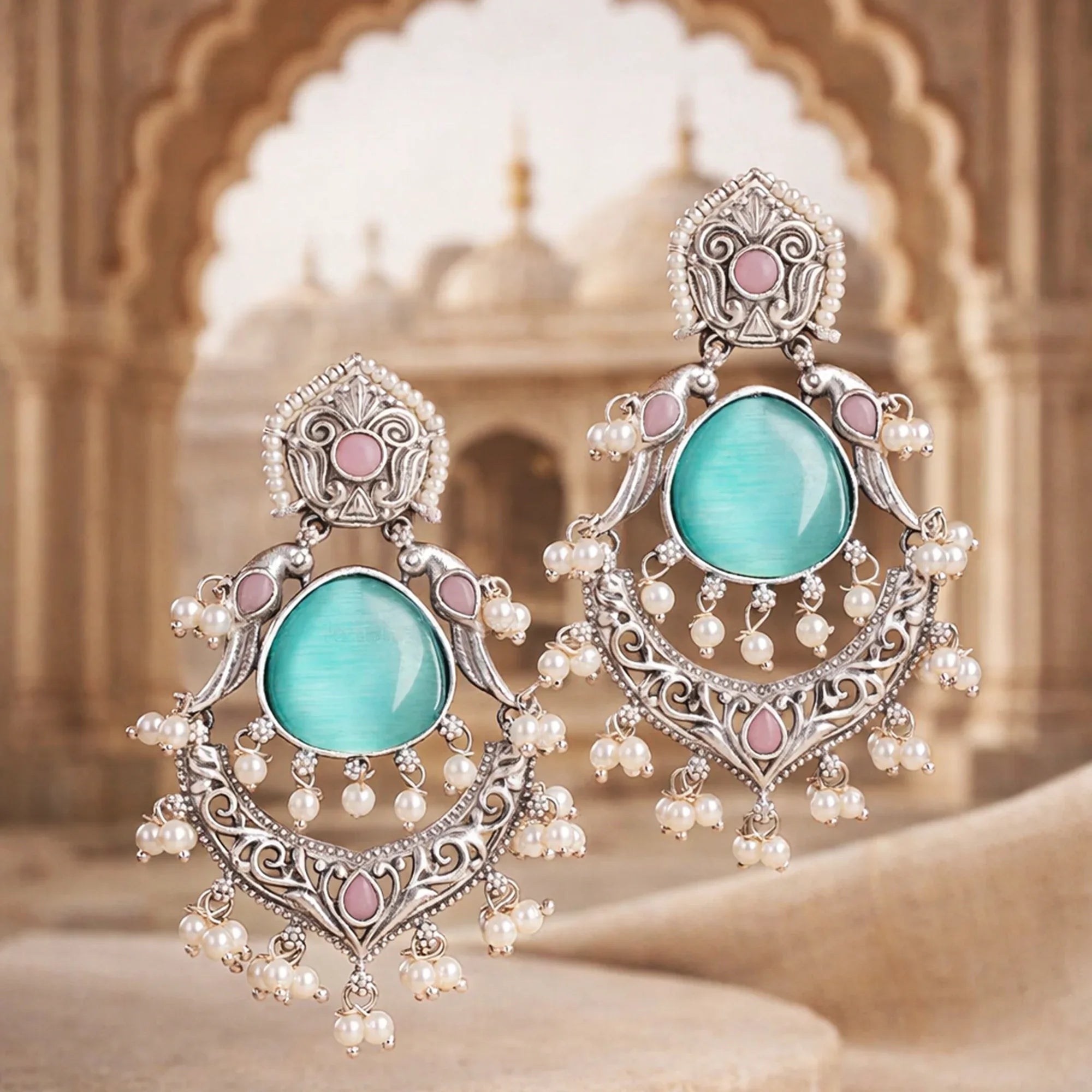 Ornate earrings with turquoise stones and pearl-like beads against a blurred architectural background