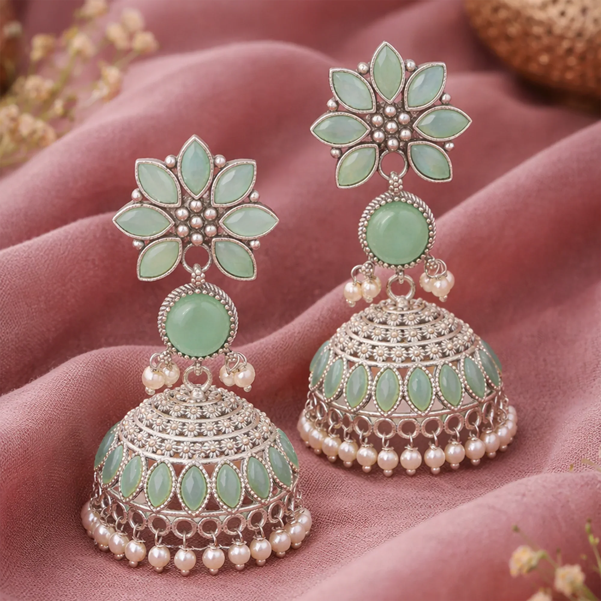 Decorative earrings with green and pearl details on a pink fabric background