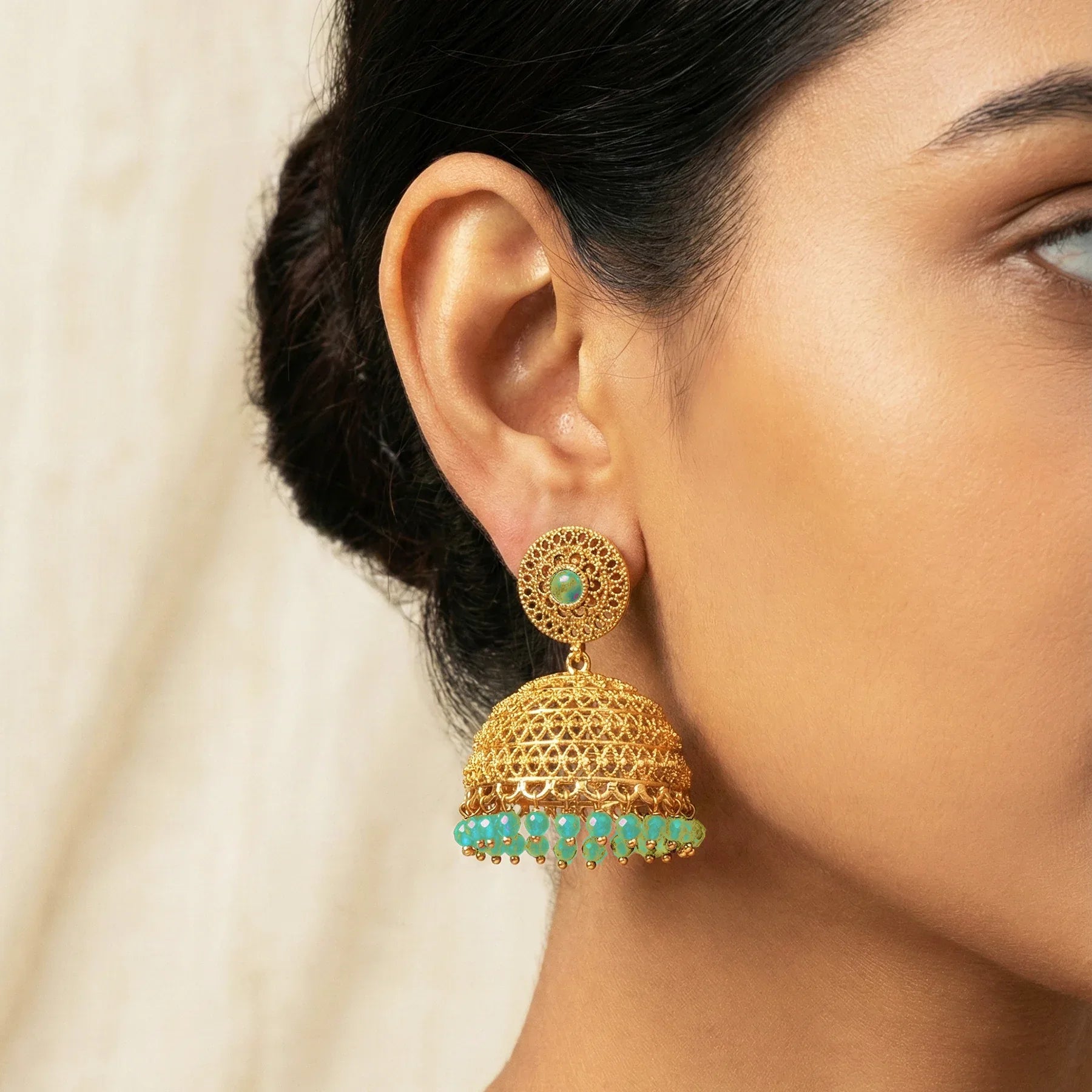 Gold and green earrings worn by a woman with a neutral background