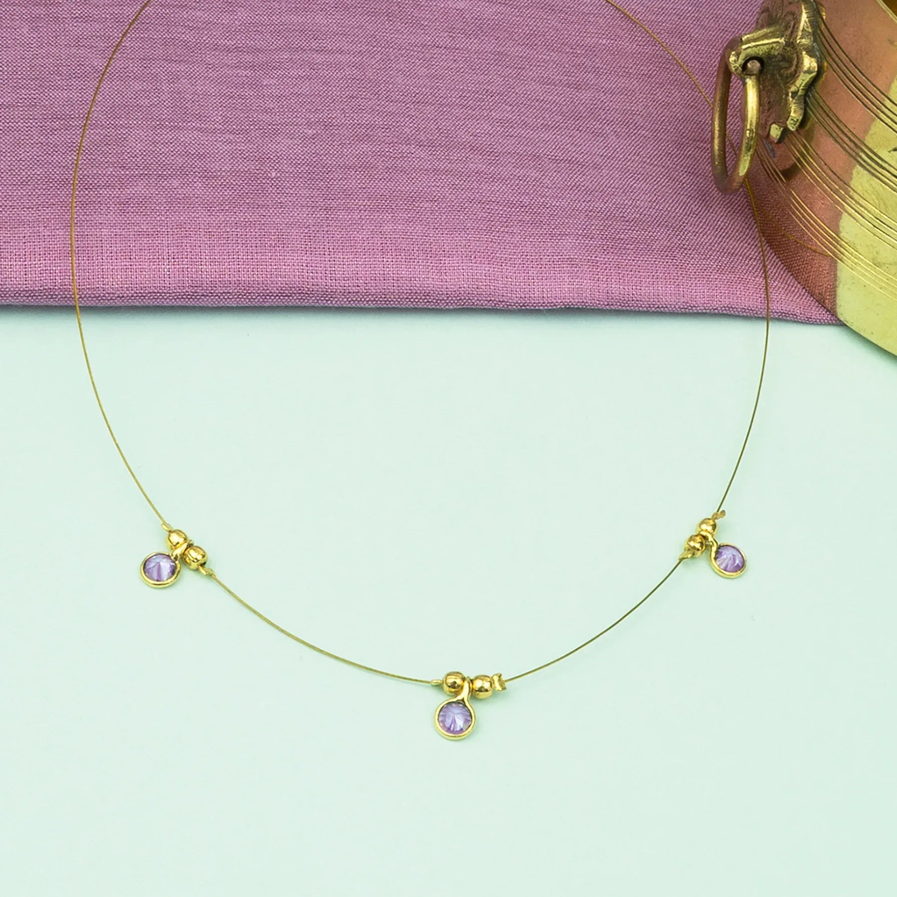 Gold necklace with purple stones on a light green surface with a pink fabric background