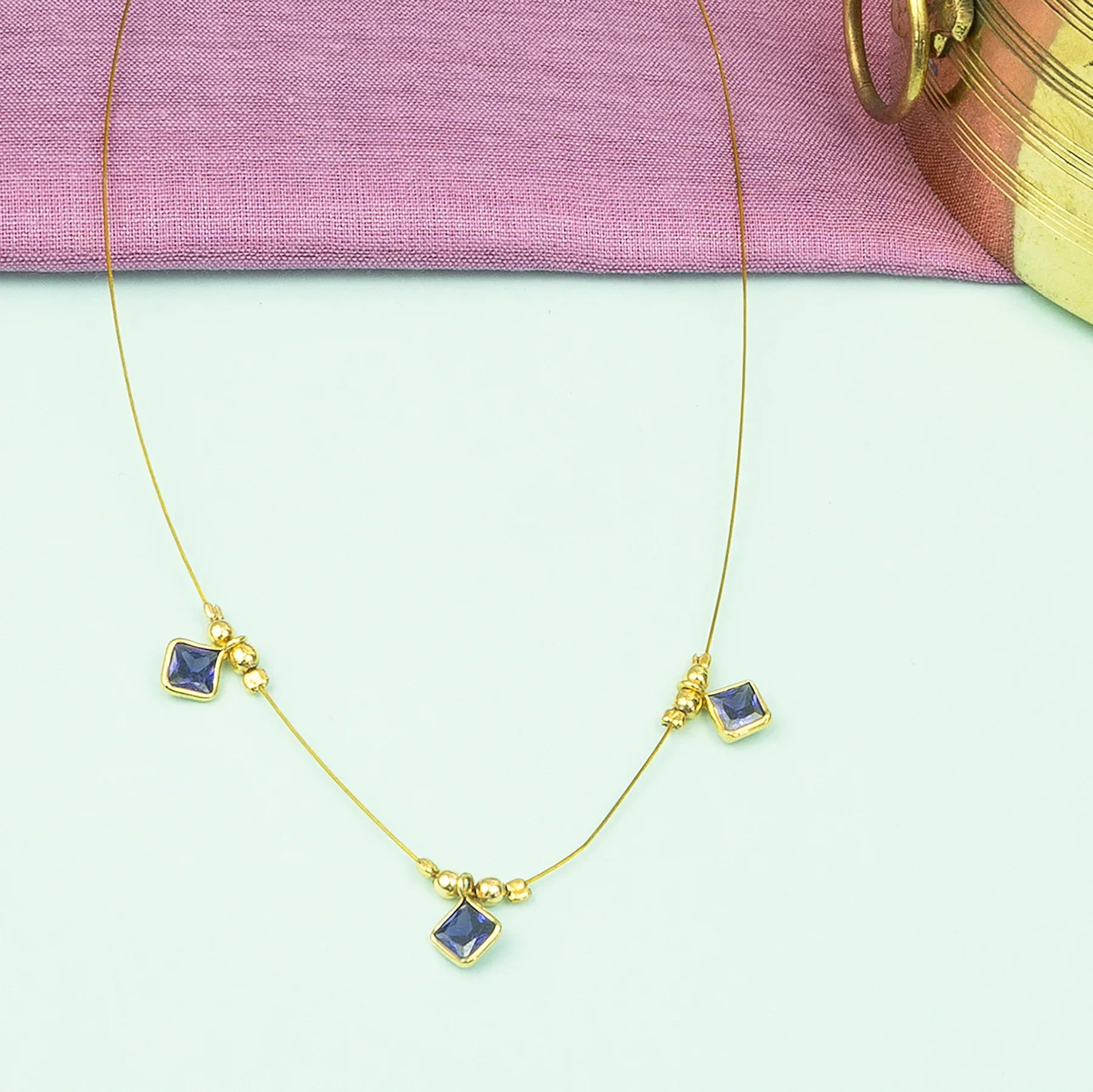 Gold necklace with blue gemstones on a light green background
