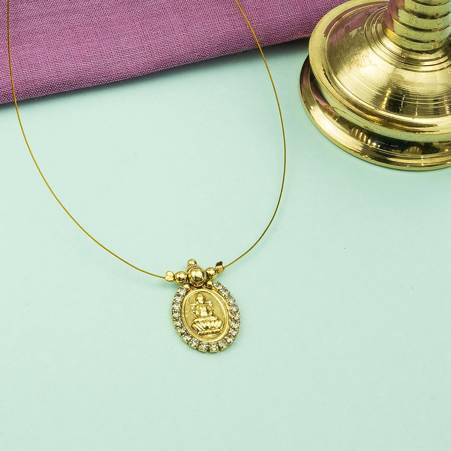 Gold necklace with a pendant on a light green surface