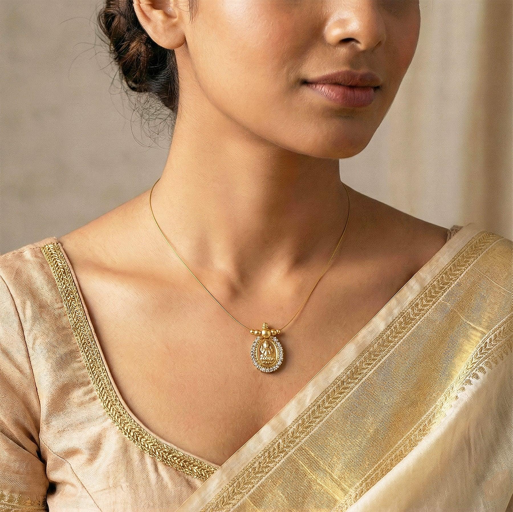 Woman wearing a gold necklace with a pendant, dressed in a cream saree.