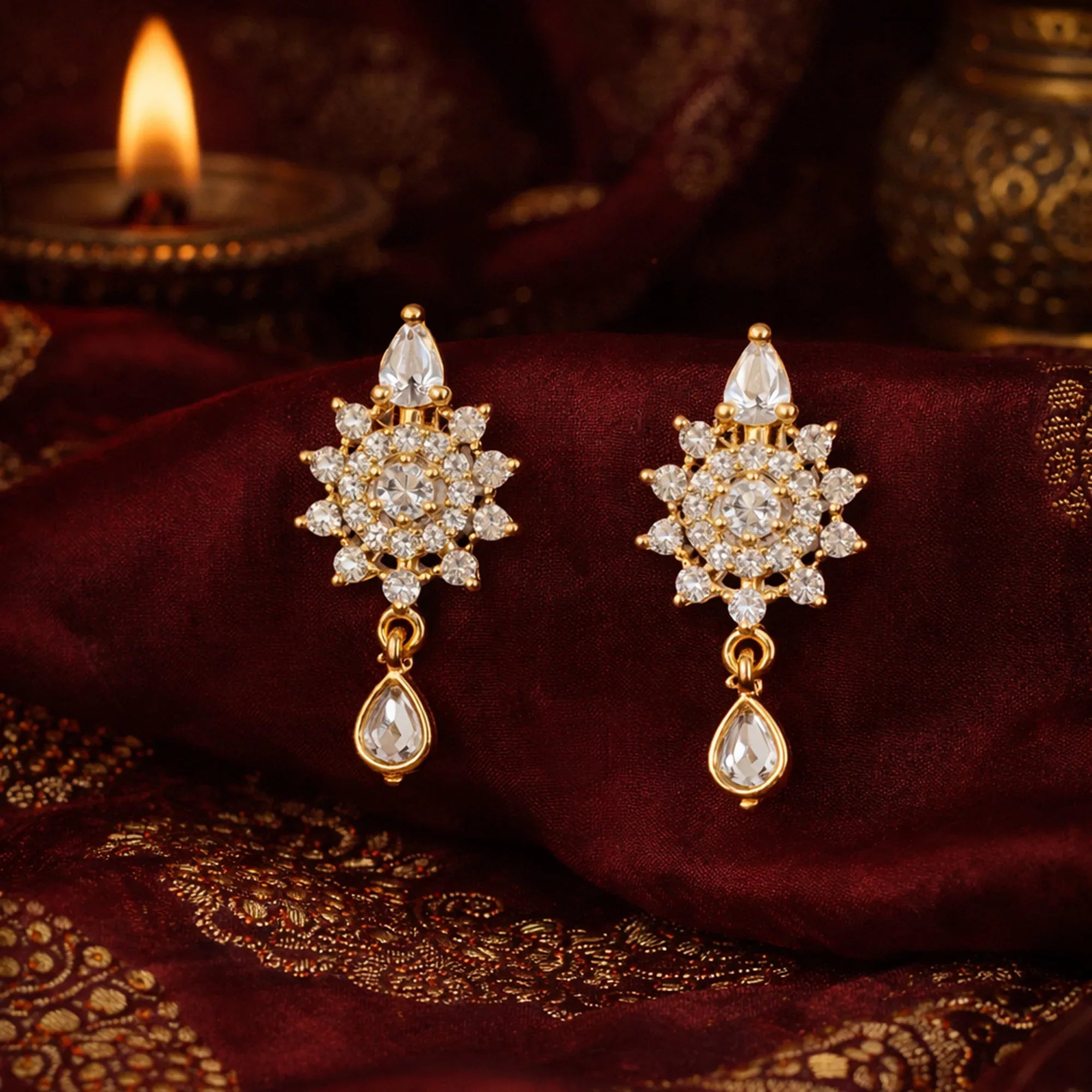 Gold and diamond earrings on a maroon fabric with a candle in the background