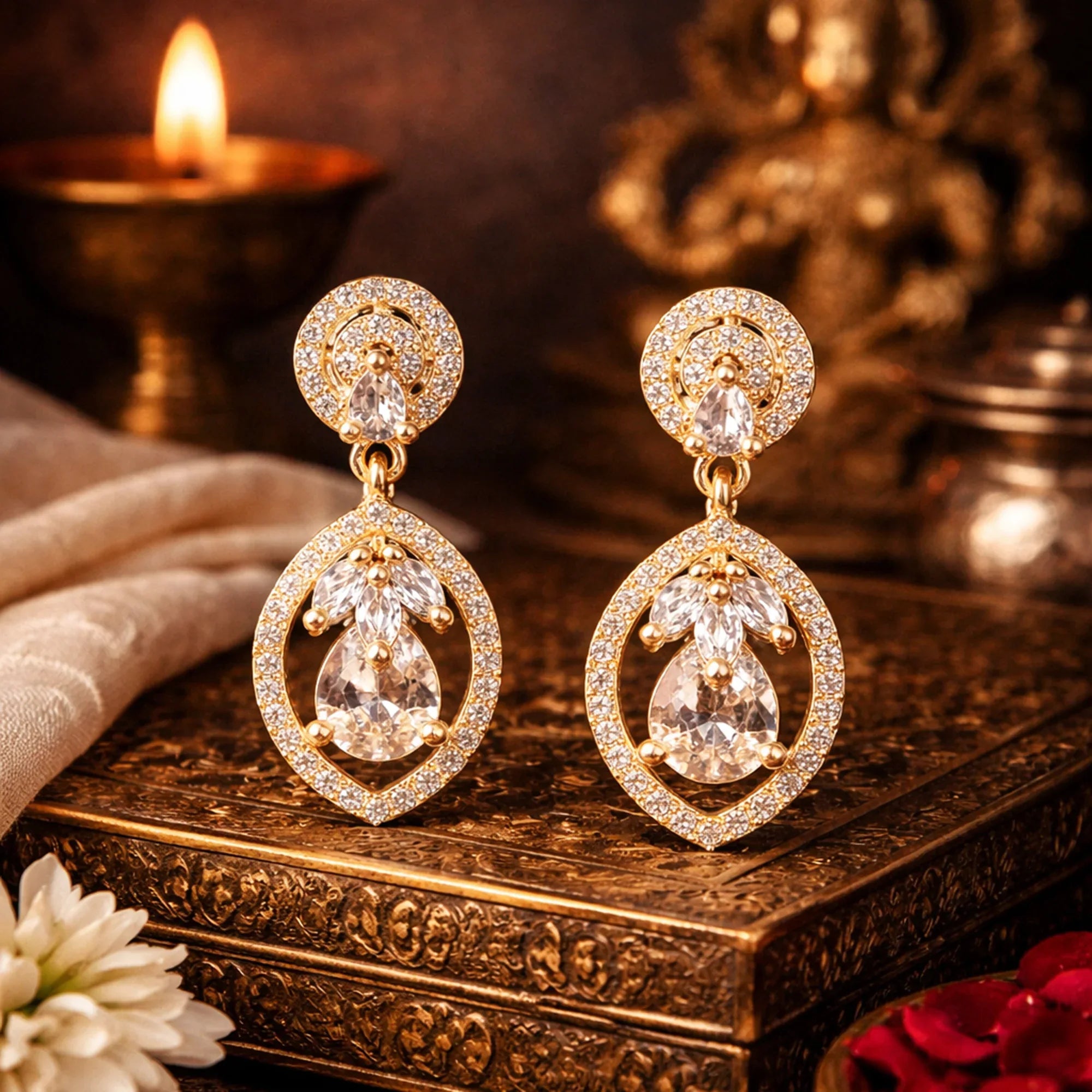 Gold earrings with clear stones on a decorative box with a candle in the background