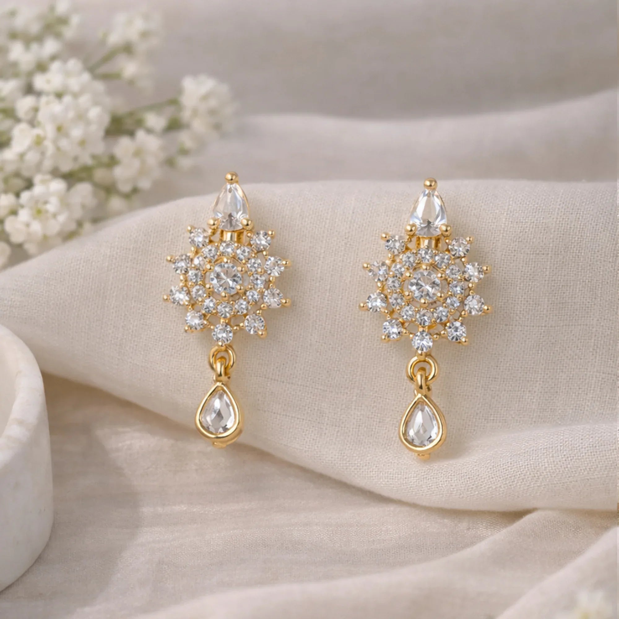 Gold earrings with diamond-like stones on a beige fabric background