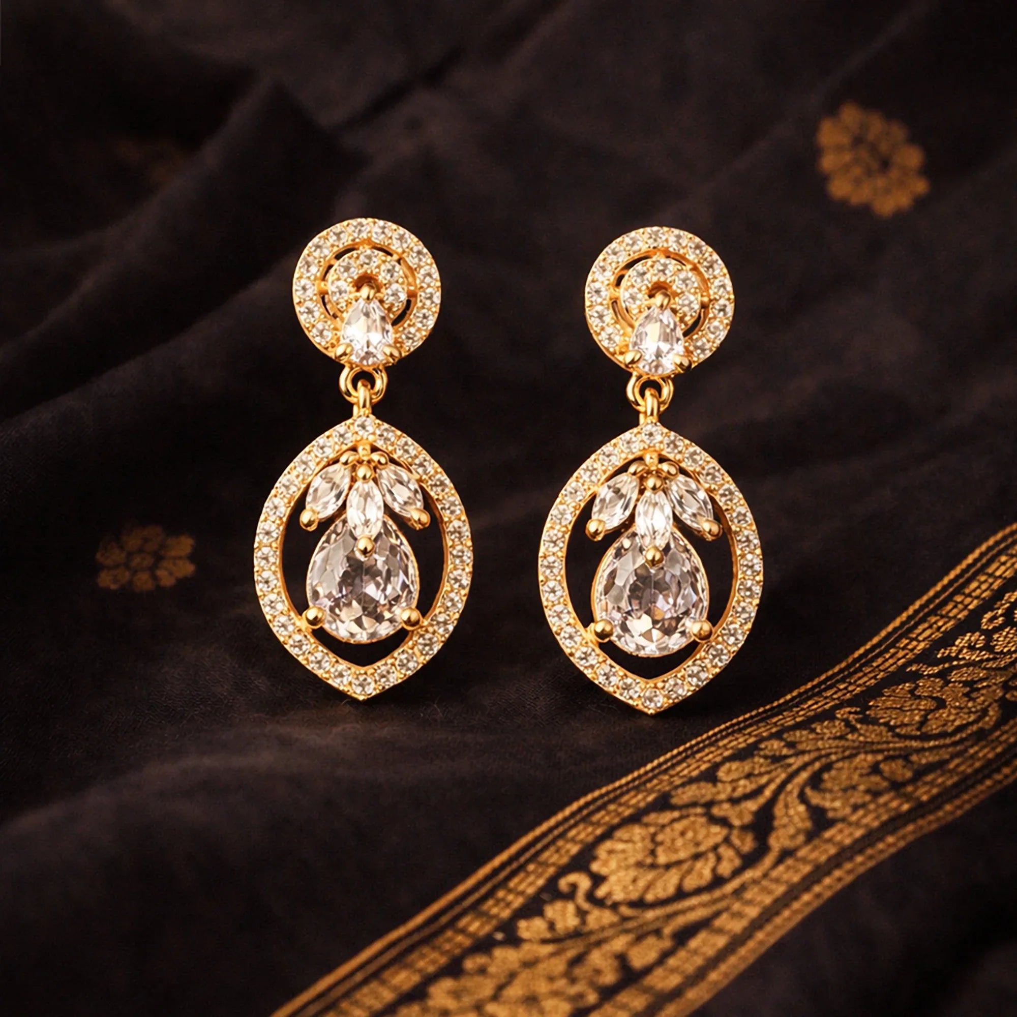 Gold earrings with clear stones on a dark fabric background