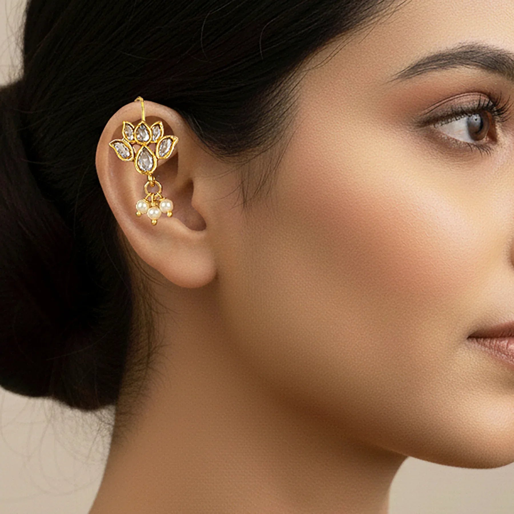 Close-up of a woman wearing a gold and pearl earring with a neutral background