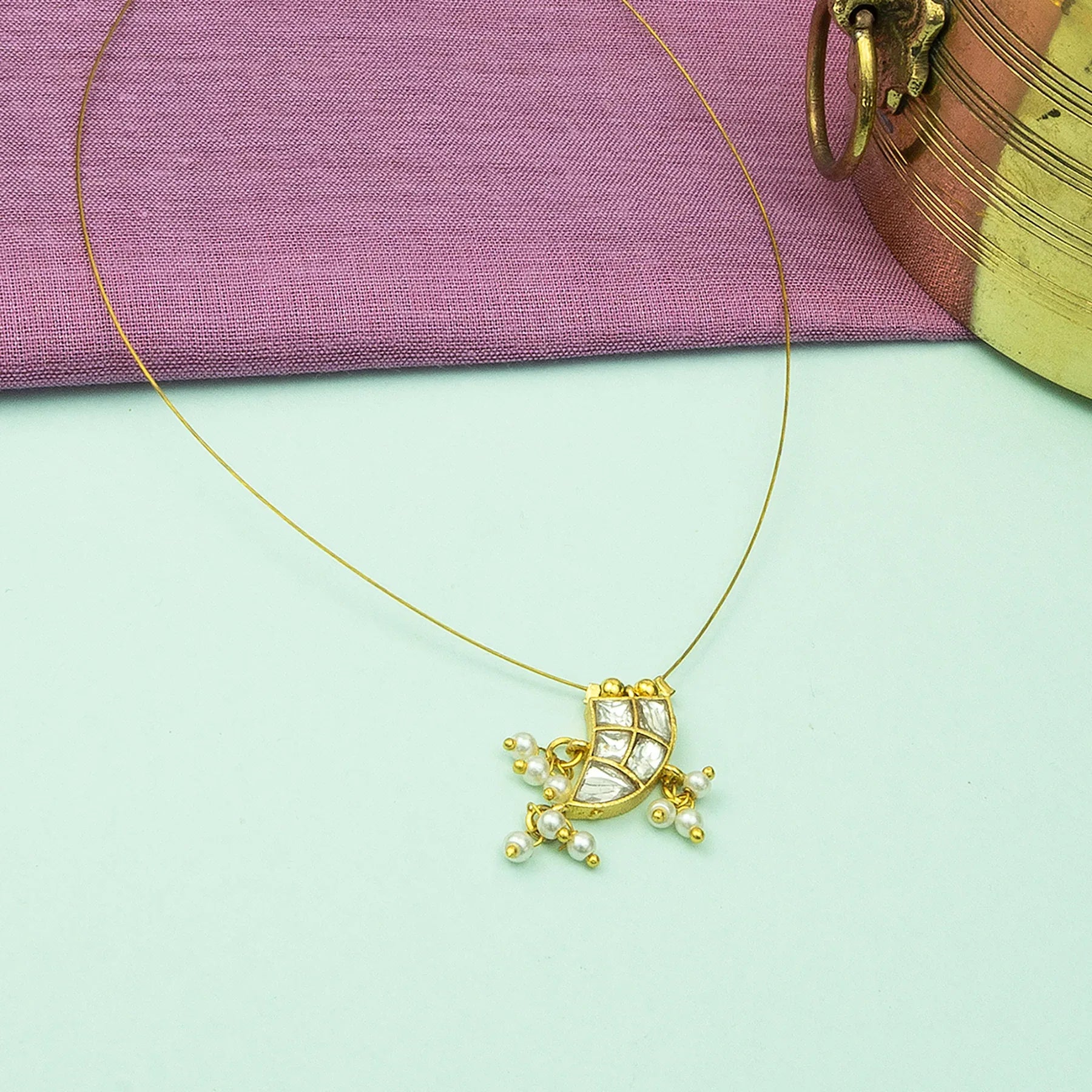Gold necklace with a decorative pendant on a light green surface