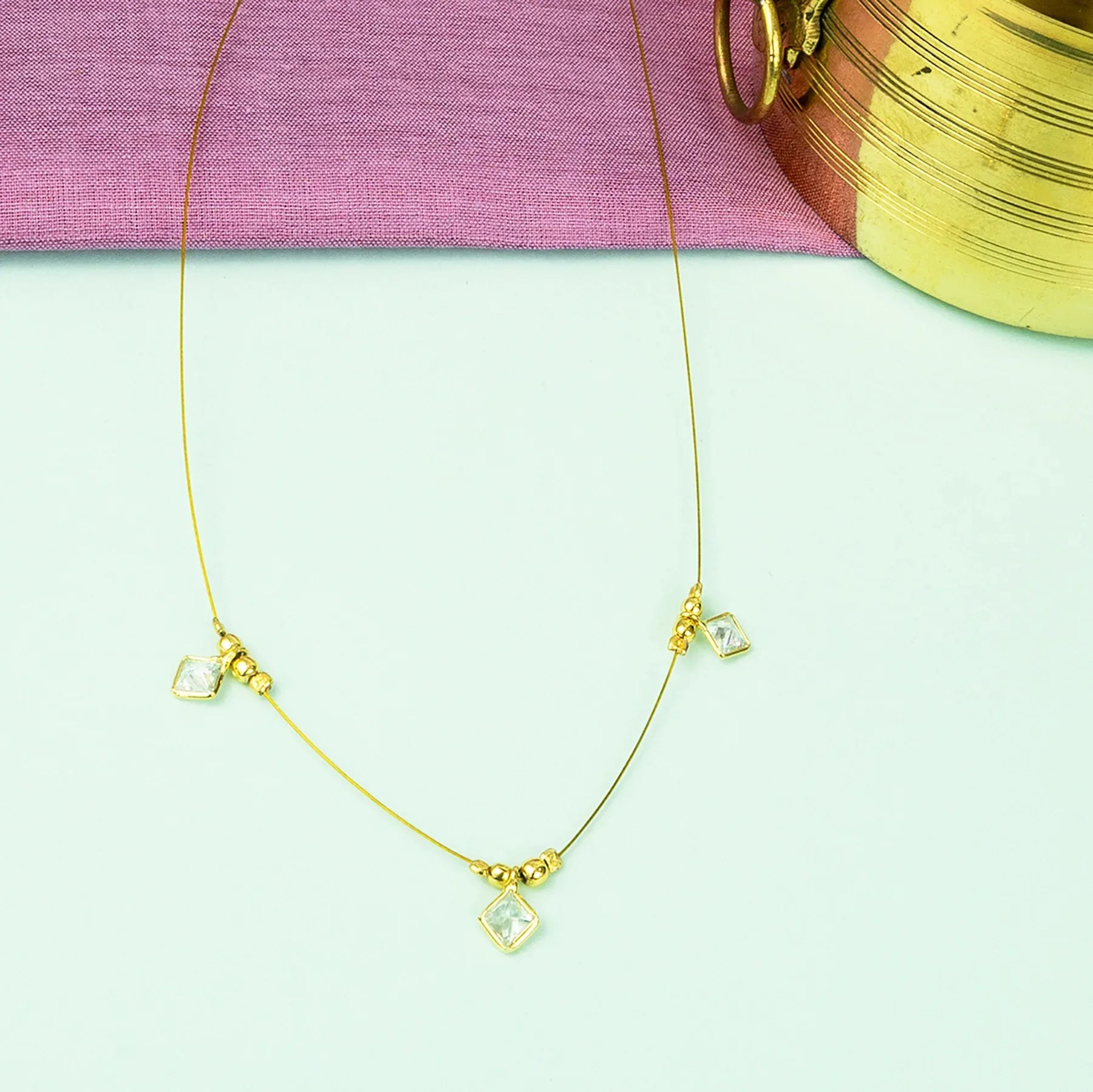 Gold necklace with clear gemstones on a light green surface with a pink fabric background