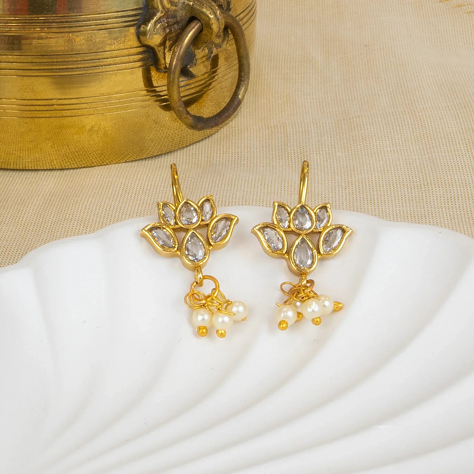 Gold earrings with pearl drops on a white shell and beige fabric background