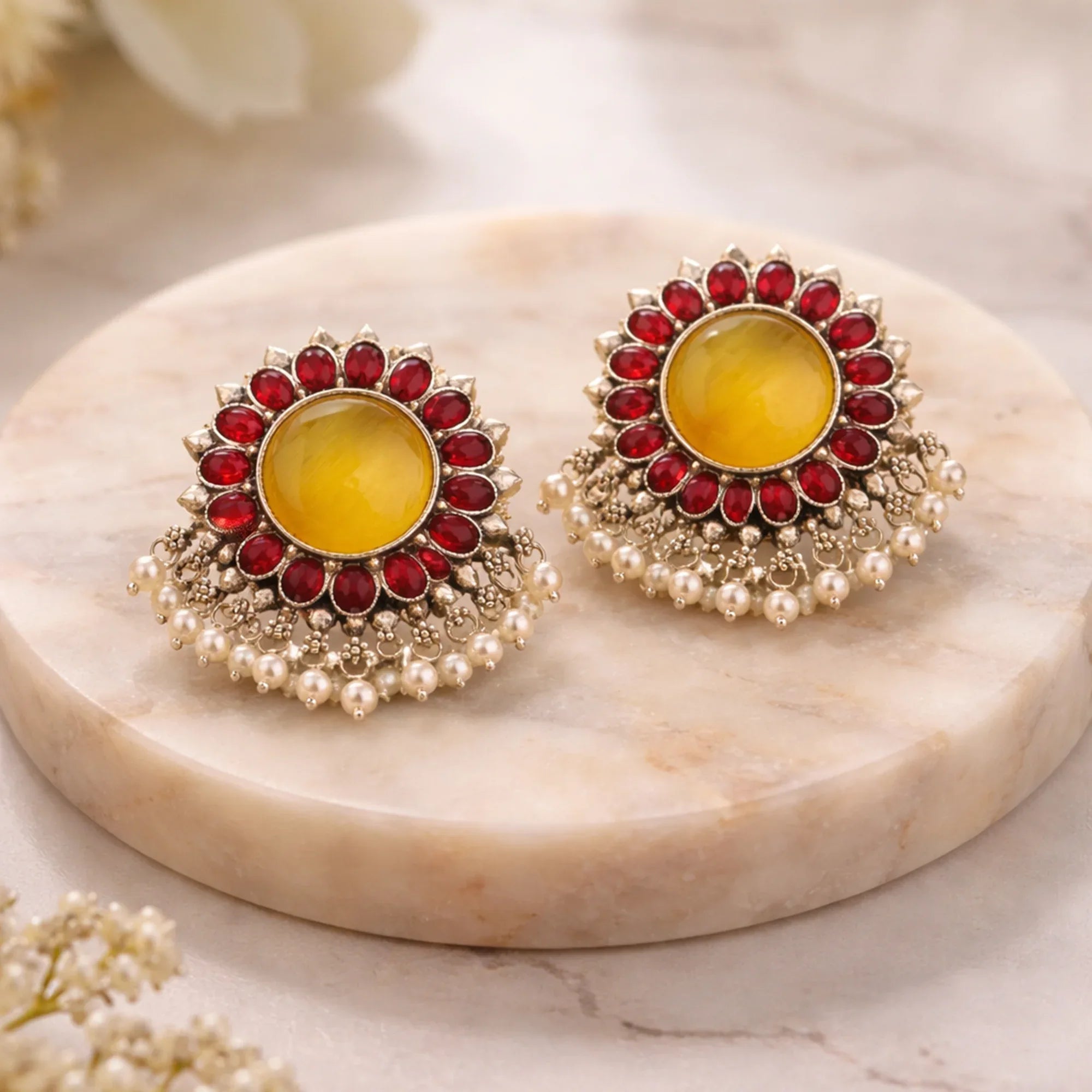 Pair of ornate earrings with yellow centers and red and gold detailing on a marble surface.