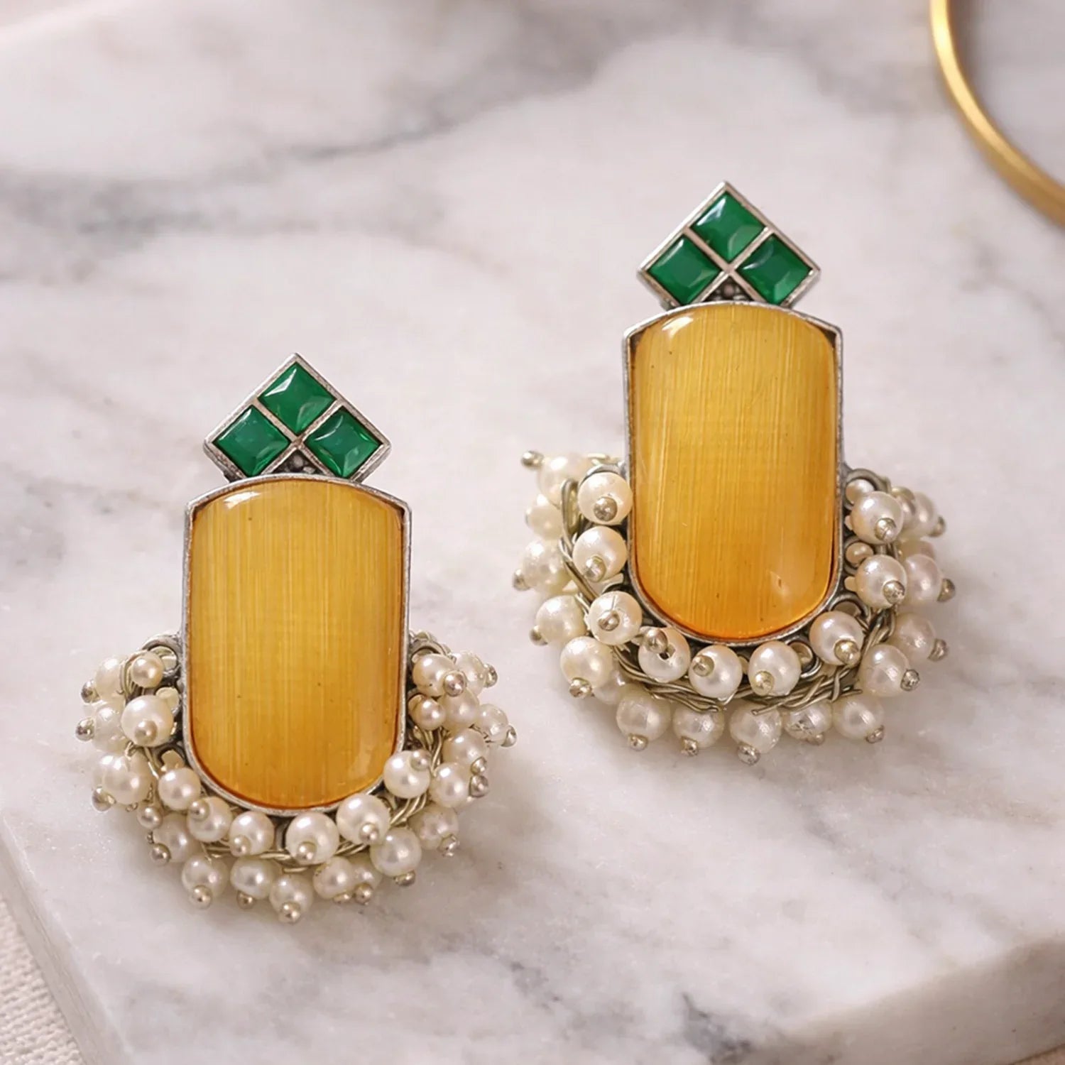 Pair of earrings with yellow center, green top, and pearl embellishments on a marble surface.