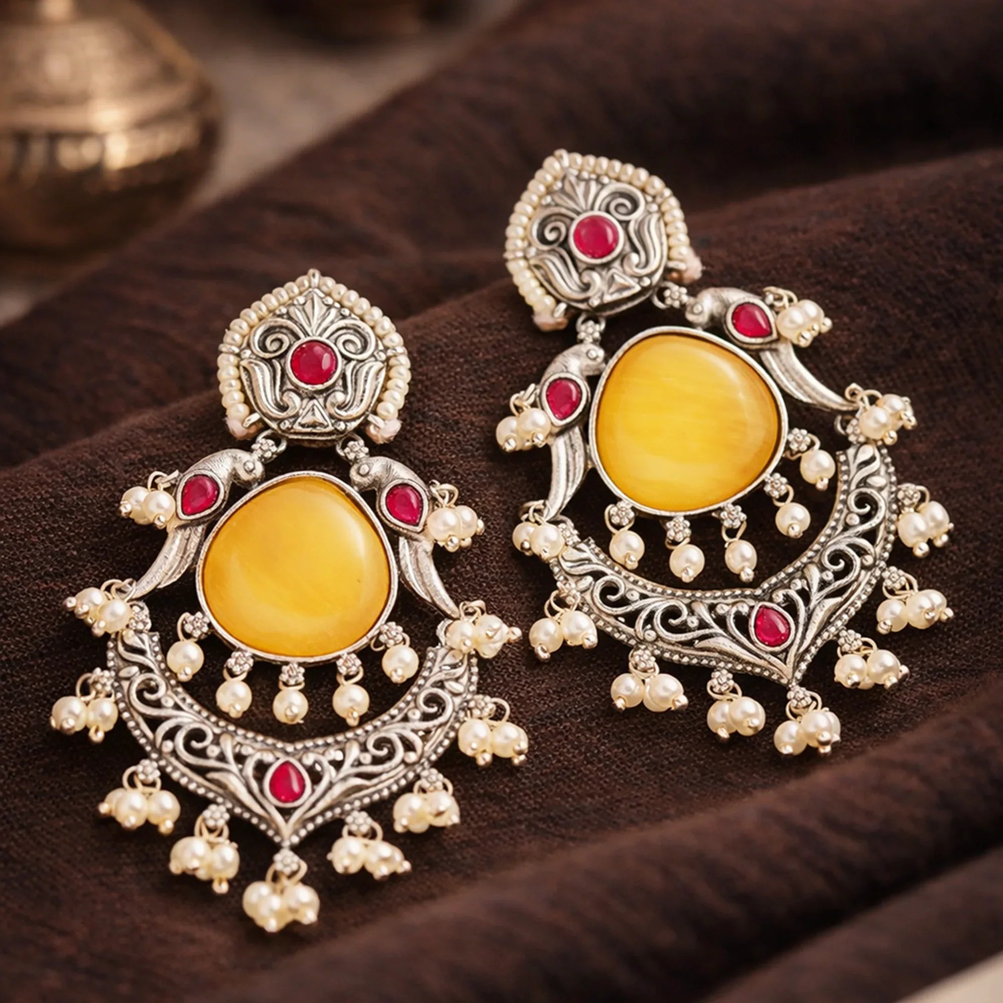 Ornate earrings with yellow stones and red gemstones on a dark surface