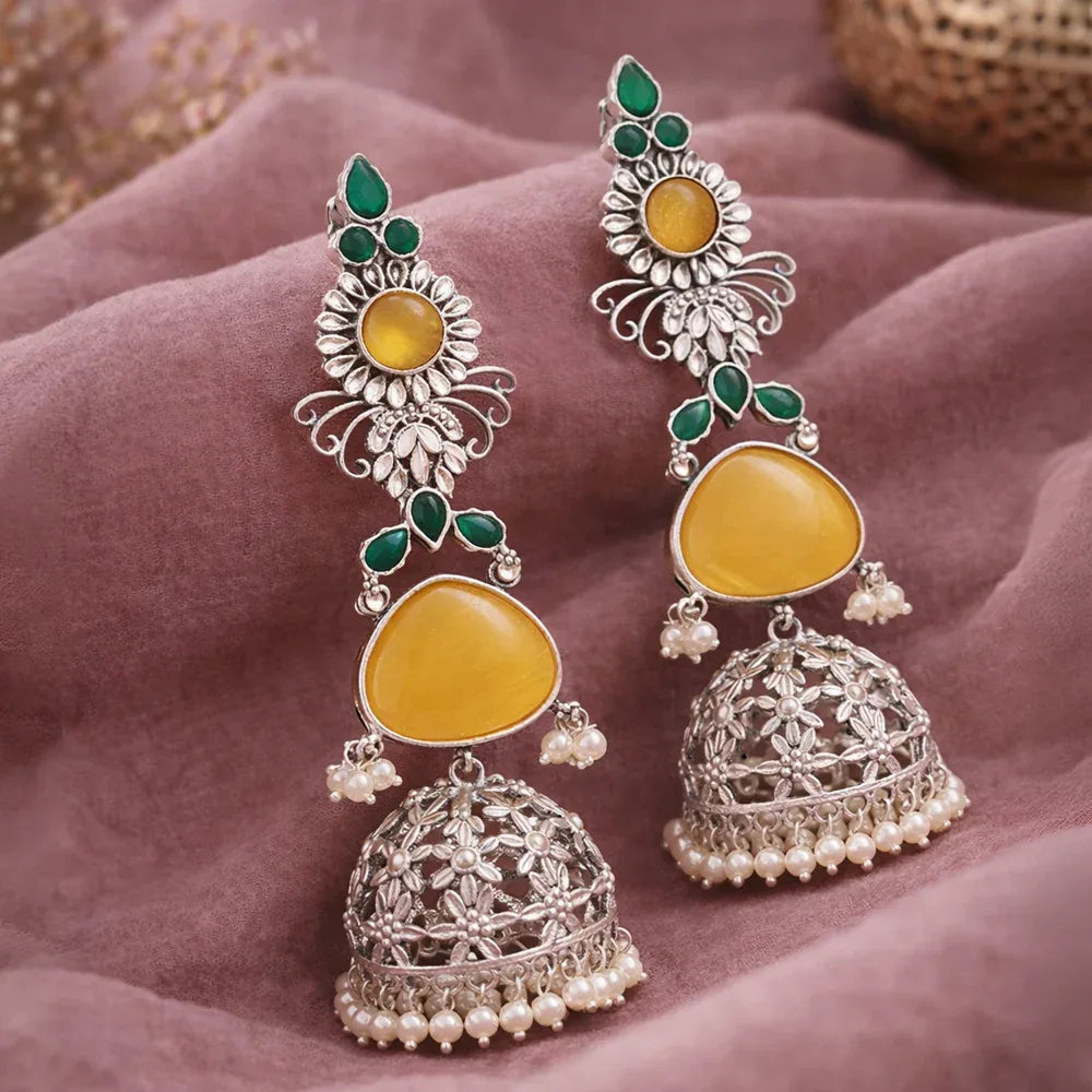 Ornate earrings with yellow stones and silver detailing on a soft fabric background