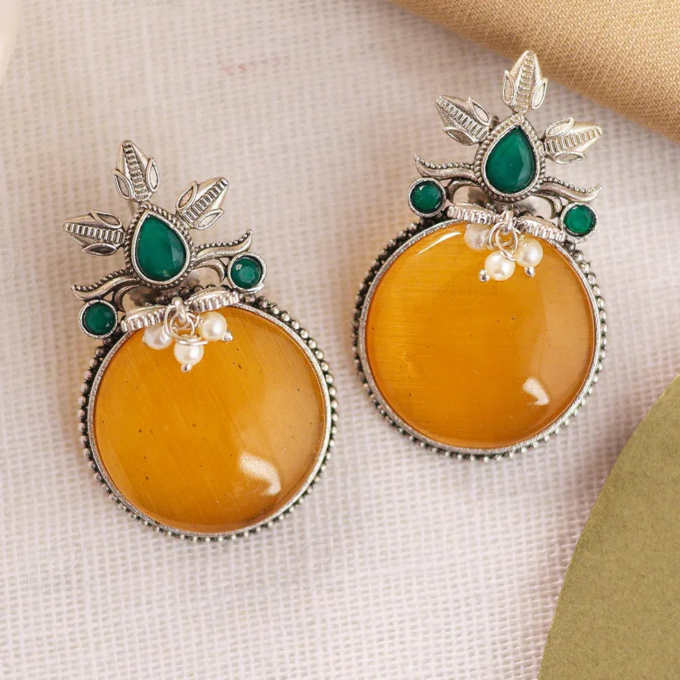 Pair of earrings with amber-like stones and green gemstones on a textured beige background